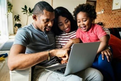 A happy family sat together looking at a laptop checking eligibility for free heating and insulation grants