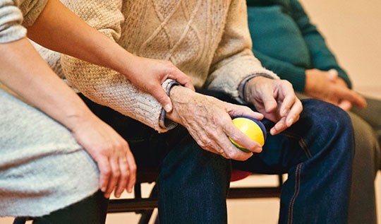 An adult holding the wrist of a vulnerable old person whilst supporting them with their cold home